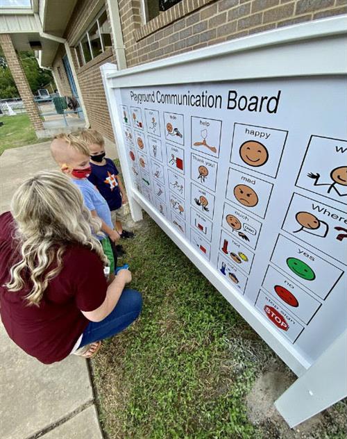 teacher and students looking at communication board 